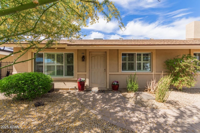 view of exterior entry with fence and stucco siding