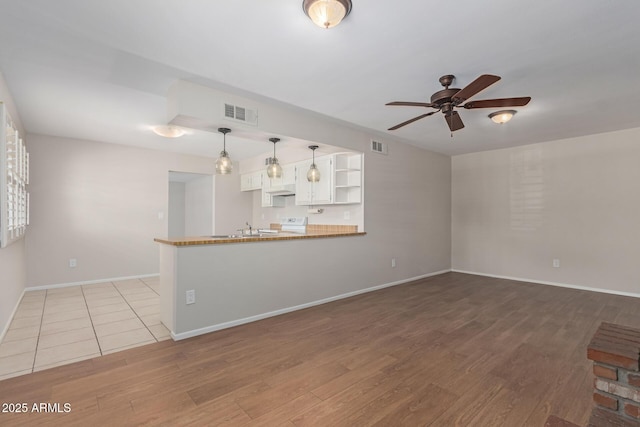 unfurnished living room with visible vents, wood finished floors, baseboards, ceiling fan, and a sink