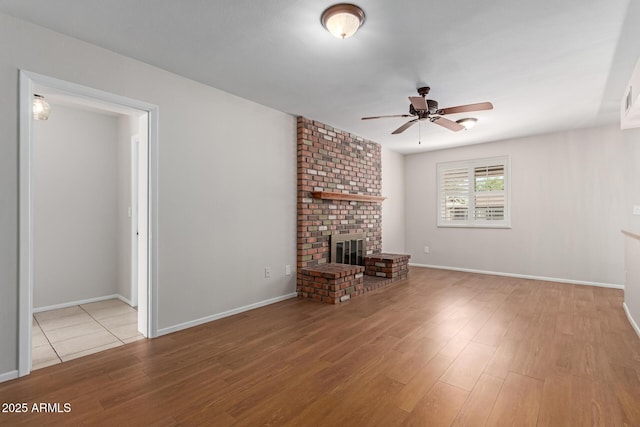 unfurnished living room with a brick fireplace, a ceiling fan, baseboards, and wood finished floors