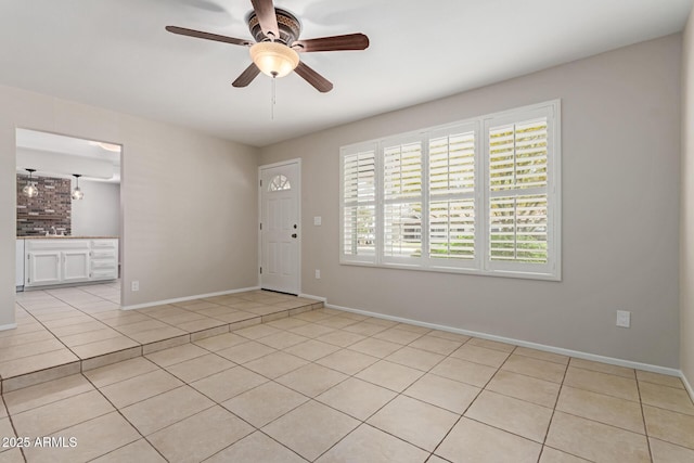 empty room featuring a ceiling fan, baseboards, and light tile patterned floors