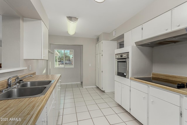 kitchen featuring black electric stovetop, light tile patterned flooring, under cabinet range hood, a sink, and stainless steel oven