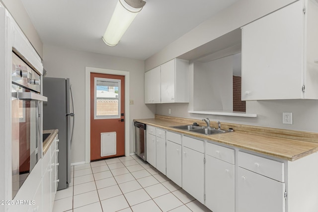 kitchen with stainless steel appliances, light countertops, light tile patterned flooring, a sink, and white cabinetry