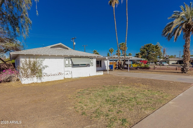 ranch-style house featuring a shingled roof, an attached carport, driveway, and a front lawn