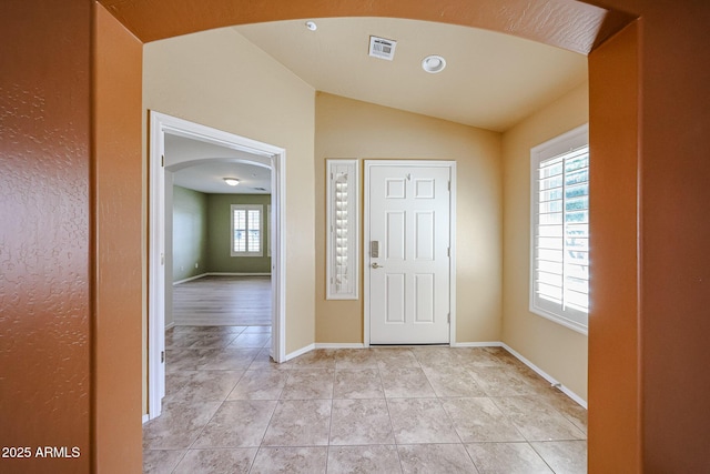 entryway with arched walkways, baseboards, light tile patterned floors, vaulted ceiling, and visible vents