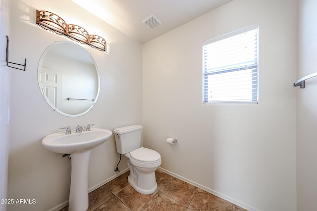 half bath with visible vents, tile patterned flooring, toilet, baseboards, and a sink