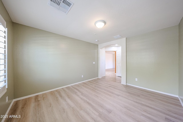 unfurnished room with visible vents, arched walkways, baseboards, and light wood-type flooring