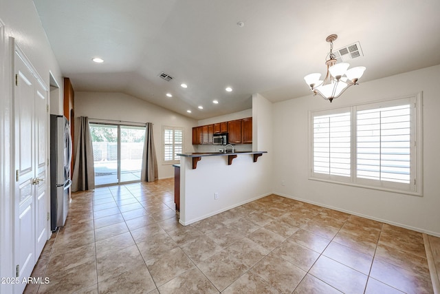 kitchen with a peninsula, lofted ceiling, a breakfast bar area, a chandelier, and appliances with stainless steel finishes