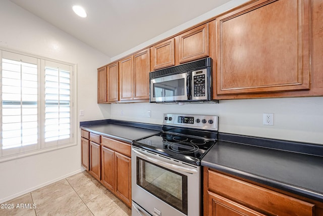 kitchen with brown cabinets, dark countertops, appliances with stainless steel finishes, light tile patterned floors, and lofted ceiling