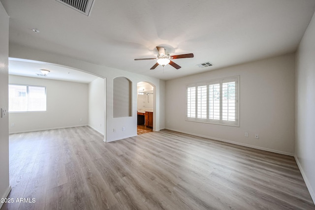 unfurnished living room featuring arched walkways, ceiling fan, light wood-style flooring, and visible vents