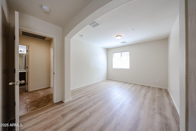 unfurnished room with arched walkways, baseboards, light wood-style flooring, and visible vents