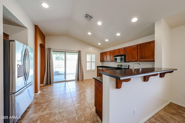 kitchen with visible vents, brown cabinetry, dark countertops, appliances with stainless steel finishes, and vaulted ceiling
