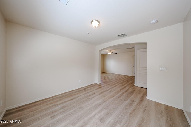 unfurnished room with visible vents, baseboards, ceiling fan, light wood-type flooring, and arched walkways