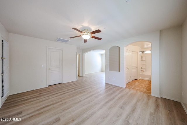 unfurnished room featuring arched walkways, ceiling fan, visible vents, and light wood-style flooring