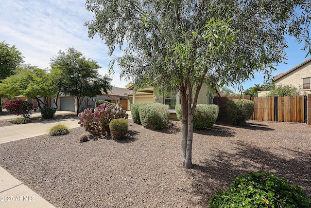 view of property hidden behind natural elements with fence, stucco siding, driveway, and a garage