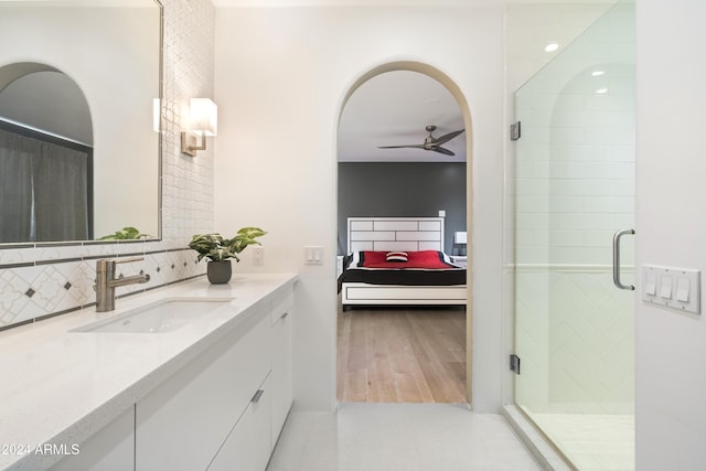 ensuite bathroom featuring decorative backsplash, a stall shower, ceiling fan, vanity, and ensuite bath