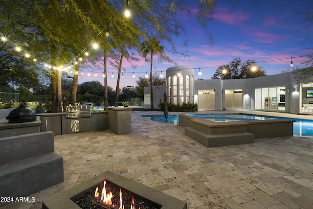 pool at dusk featuring a fire pit, area for grilling, an in ground hot tub, a grill, and a patio area