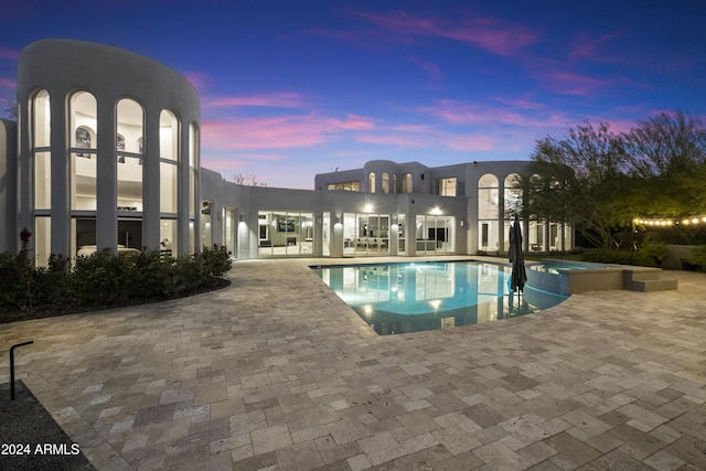 pool at dusk featuring a patio area and an in ground hot tub