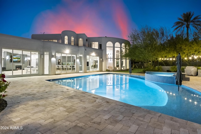 pool at dusk with an in ground hot tub and a patio