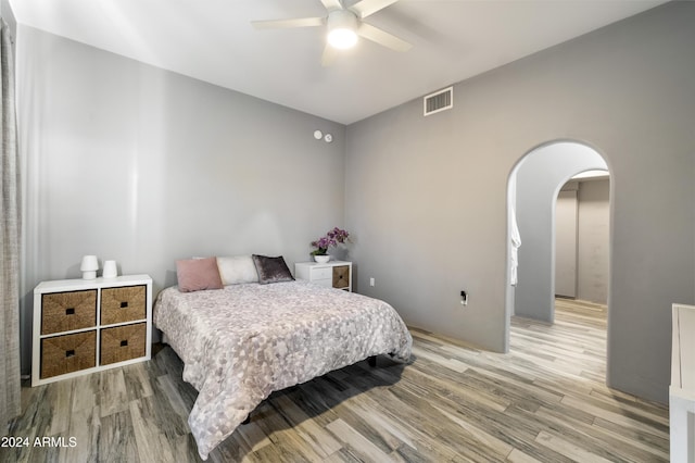 bedroom featuring arched walkways, light wood-style flooring, visible vents, and a ceiling fan