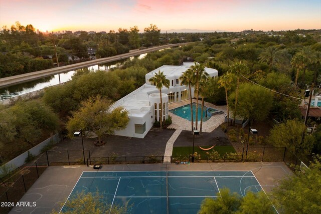 pool at dusk featuring a water view and tennis court