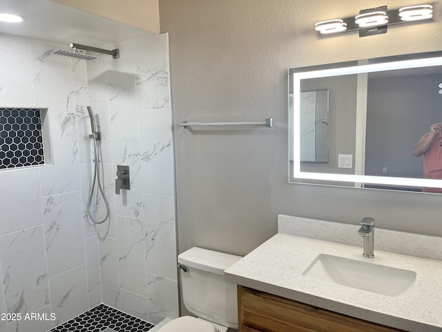 bathroom featuring vanity, toilet, and a tile shower