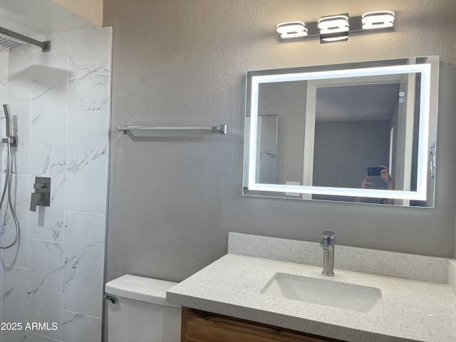 bathroom with tiled shower, vanity, and toilet