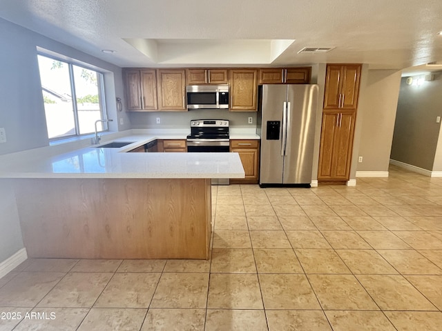 kitchen with sink, light tile patterned floors, appliances with stainless steel finishes, a tray ceiling, and kitchen peninsula