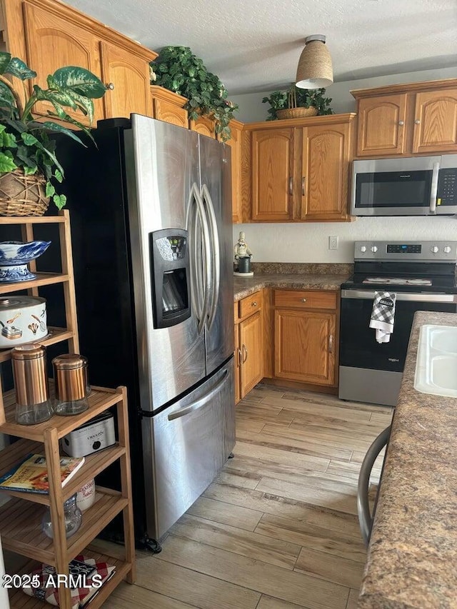 kitchen featuring light hardwood / wood-style floors, a textured ceiling, and appliances with stainless steel finishes