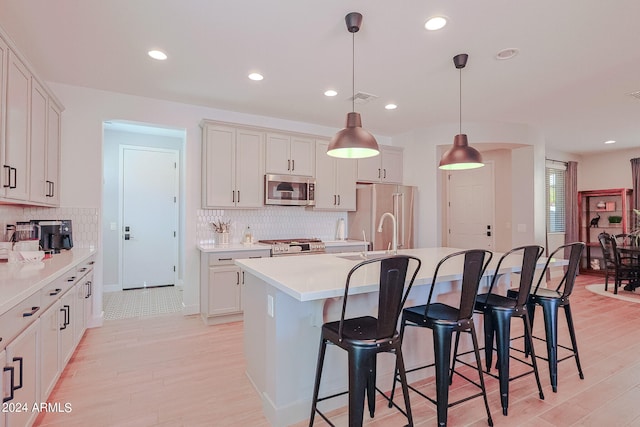 kitchen featuring appliances with stainless steel finishes, a center island with sink, light hardwood / wood-style flooring, and decorative light fixtures