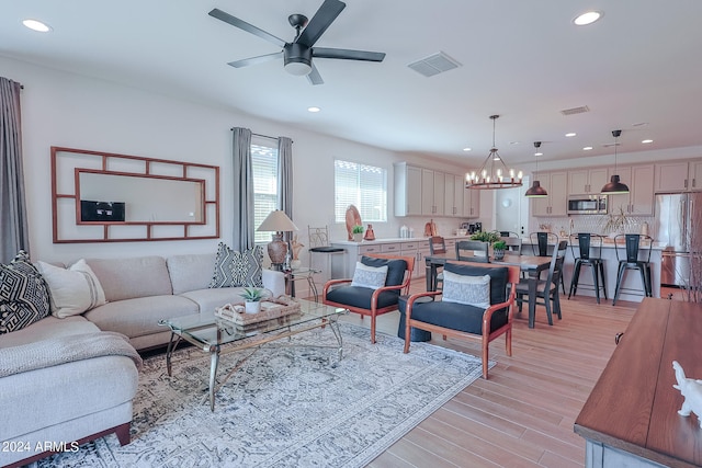 living room with ceiling fan with notable chandelier and light hardwood / wood-style flooring