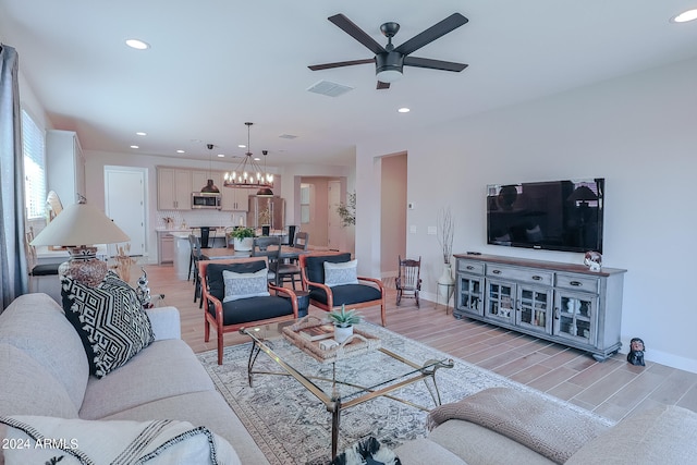 living room featuring ceiling fan with notable chandelier and light wood-type flooring