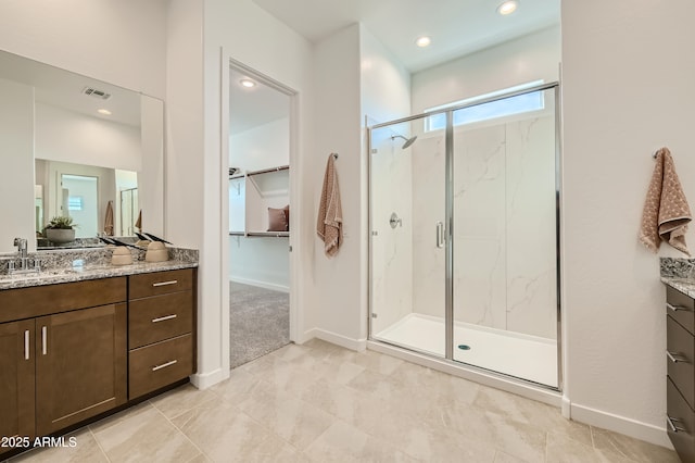 full bathroom with a marble finish shower, baseboards, visible vents, a walk in closet, and vanity