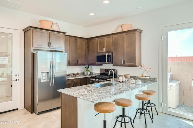 kitchen featuring a peninsula, a sink, visible vents, appliances with stainless steel finishes, and light stone countertops