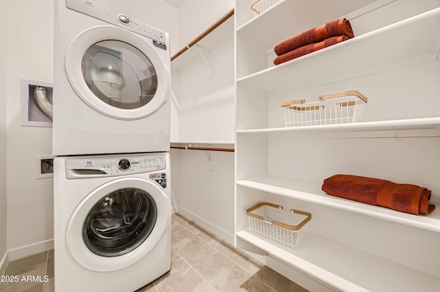 clothes washing area featuring stacked washer / dryer, laundry area, light tile patterned flooring, and baseboards