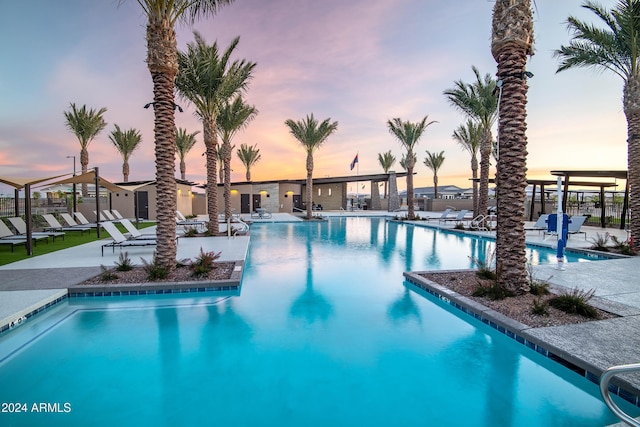 pool at dusk featuring a patio area, fence, and a community pool