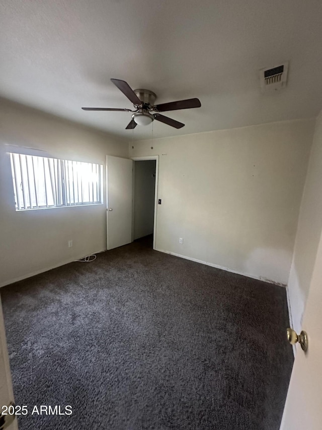 spare room with visible vents, dark colored carpet, and a ceiling fan