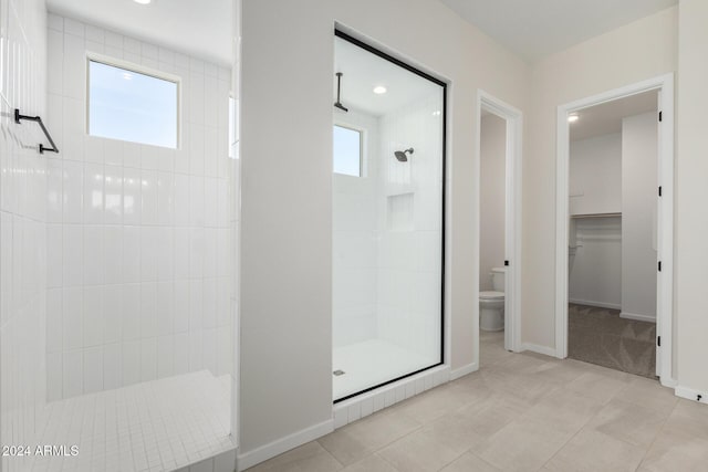 bathroom with toilet, tile patterned flooring, and tiled shower