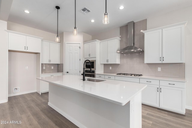 kitchen with sink, wall chimney range hood, pendant lighting, a center island with sink, and white cabinetry