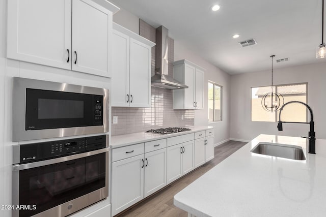 kitchen with wall chimney exhaust hood, stainless steel appliances, sink, decorative light fixtures, and an inviting chandelier