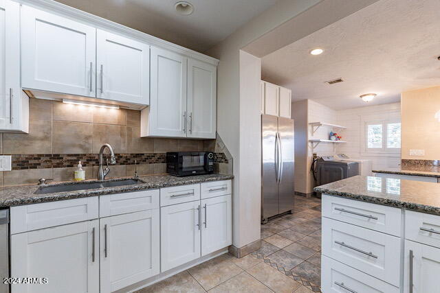 kitchen featuring white cabinets, appliances with stainless steel finishes, dark stone counters, washing machine and clothes dryer, and sink