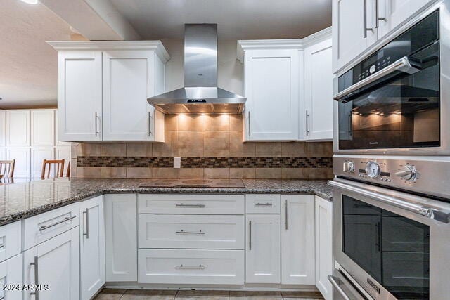 kitchen with decorative backsplash, white cabinets, wall chimney exhaust hood, and dark stone counters