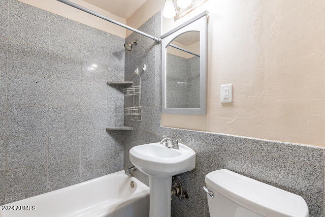 bathroom with tiled shower / bath combo, toilet, and tile walls