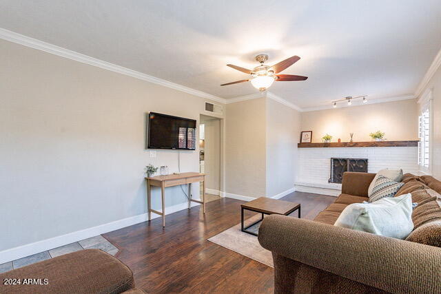 living room featuring ceiling fan, dark wood-type flooring, crown molding, and a fireplace