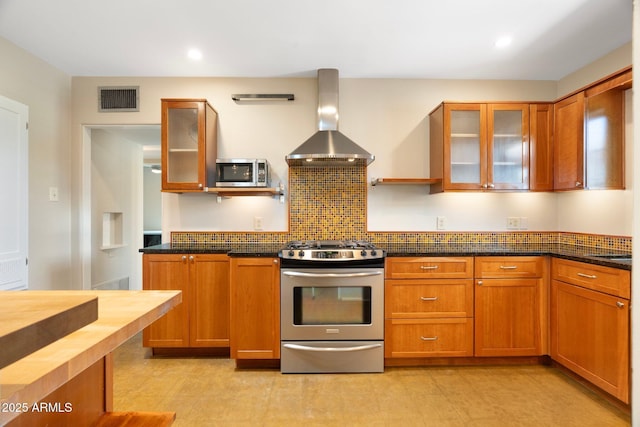 kitchen featuring backsplash, wall chimney range hood, stainless steel appliances, and dark stone countertops