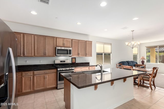 kitchen with appliances with stainless steel finishes, pendant lighting, sink, dark stone counters, and a kitchen island with sink