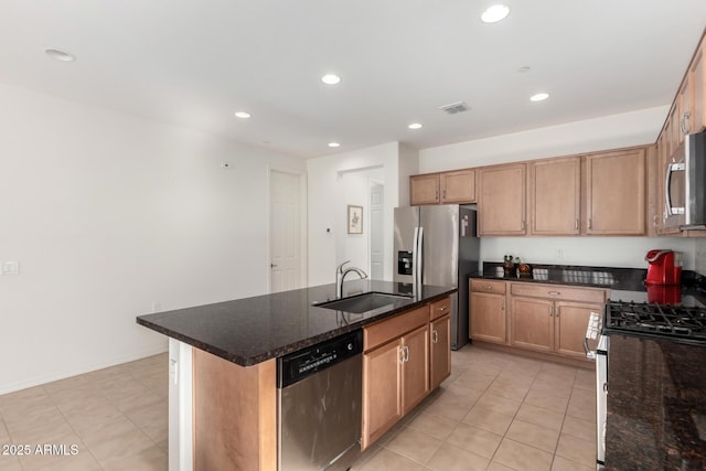 kitchen with sink, appliances with stainless steel finishes, a kitchen island with sink, dark stone countertops, and light tile patterned flooring