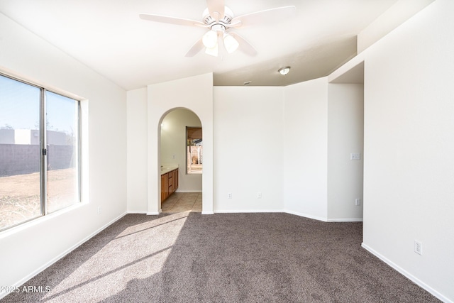 carpeted spare room with baseboards, arched walkways, and ceiling fan