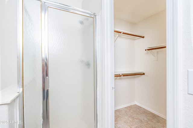 bathroom featuring a walk in closet, baseboards, and a stall shower