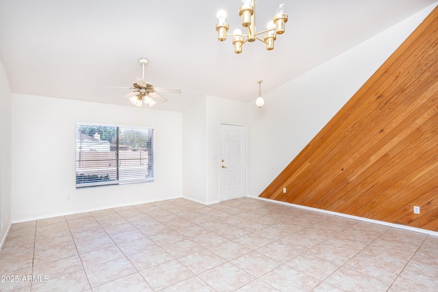 unfurnished room featuring wooden walls, light tile patterned flooring, ceiling fan with notable chandelier, and baseboards