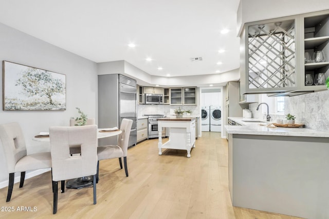 kitchen with independent washer and dryer, high end appliances, light hardwood / wood-style flooring, backsplash, and sink